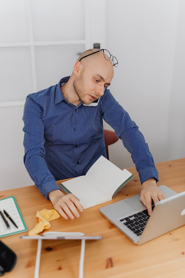 Businessman multitasking with laptop and notebook at office desk, depicting remote work dynamics.