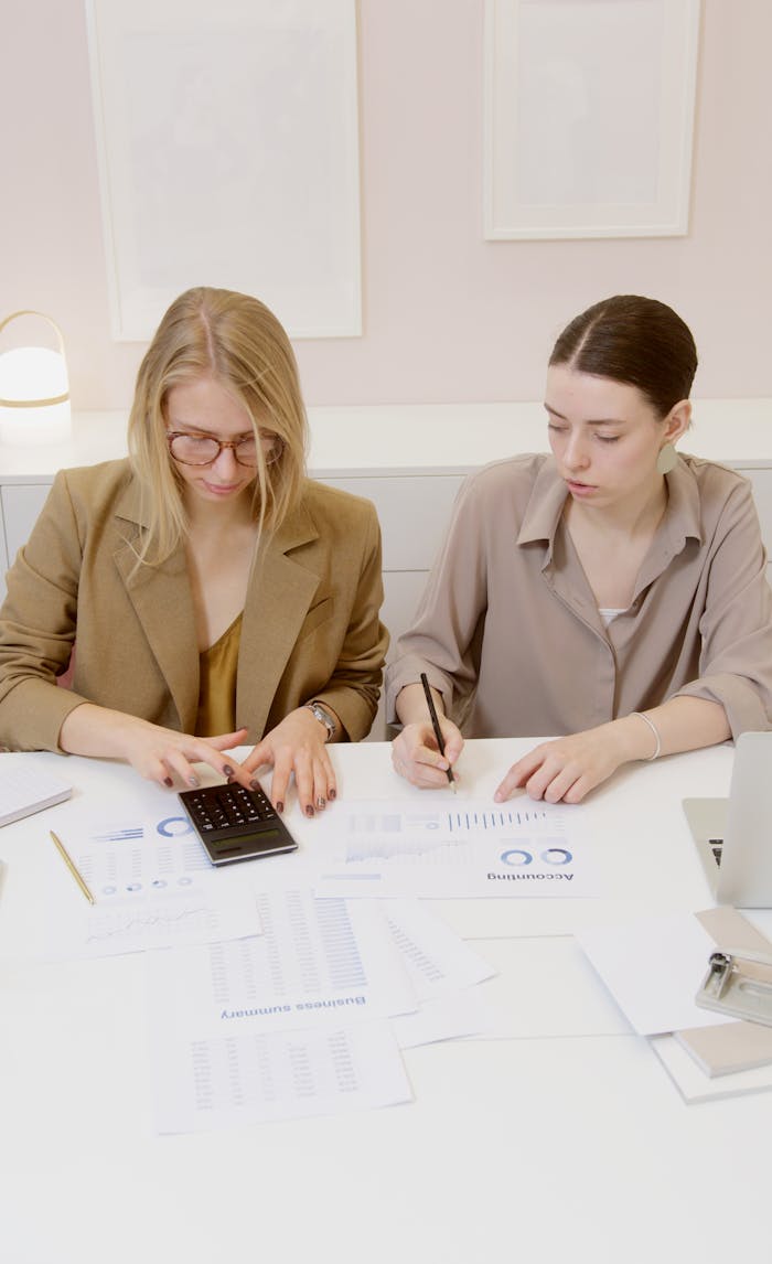 Two women working on financial documents and calculations in an office.